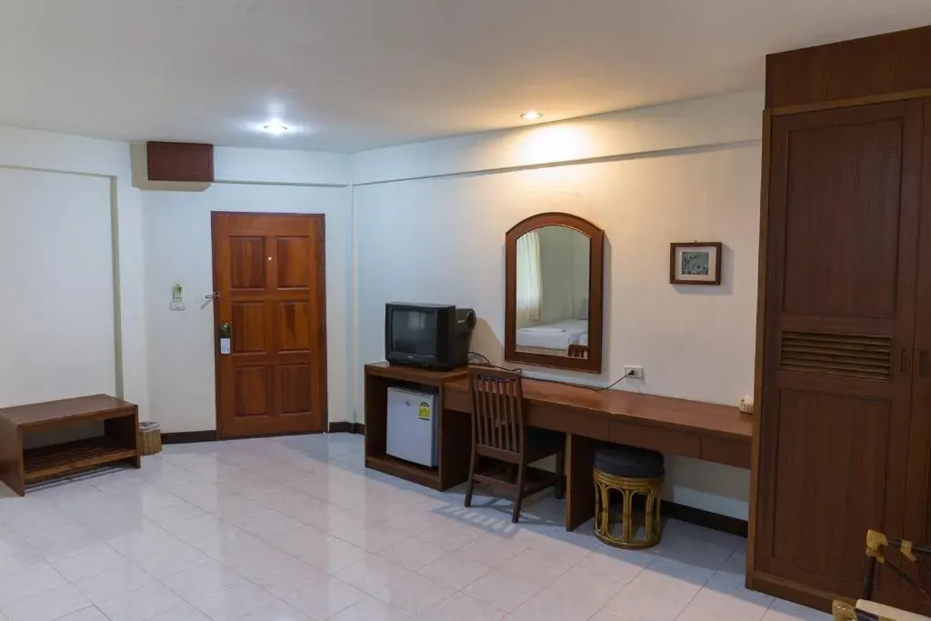 Guest room interior at Forum House Hotel with wooden furniture, desk, cable TV, and mini-fridge